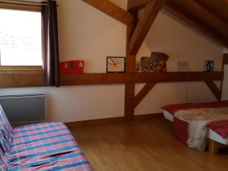 Cozy attic bedroom with wooden beams, featuring a comfortable sofa bed and a single bed, perfect for a relaxing getaway.
