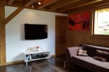 Cozy chalet living room with exposed wooden beams, a flat-screen TV, and a comfortable couch.