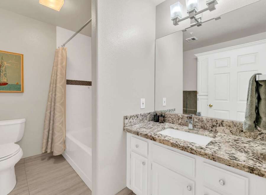 This beautiful bathroom features a modern design with a granite countertop and white cabinetry.