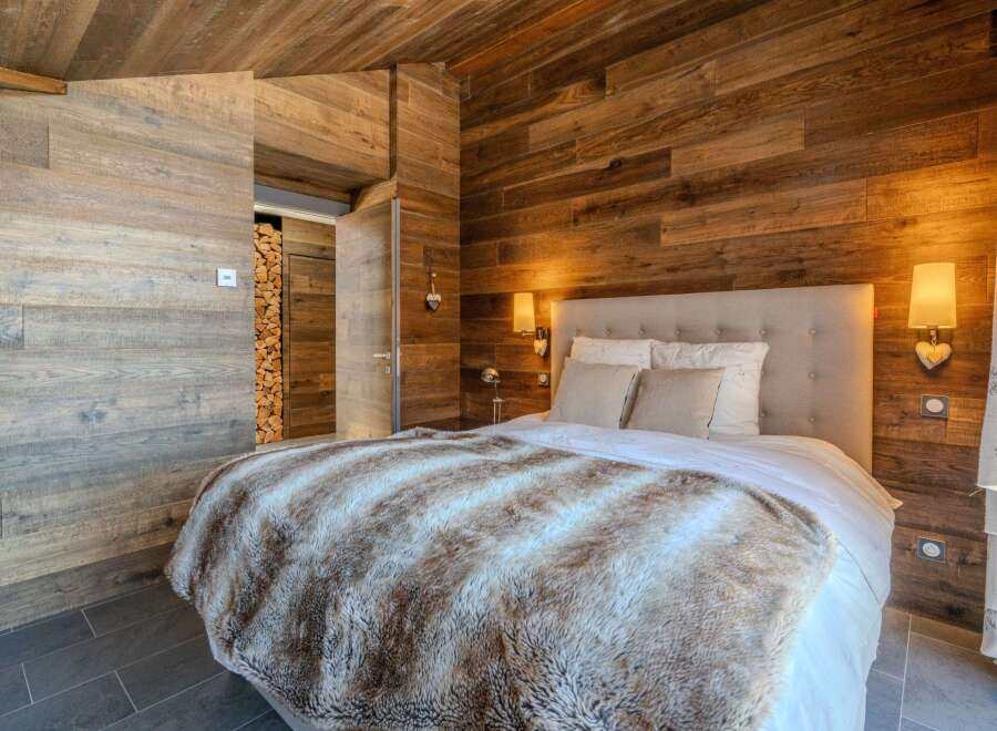 Experience rustic charm in this cozy bedroom featuring stunning wood paneling and a luxurious faux fur blanket.