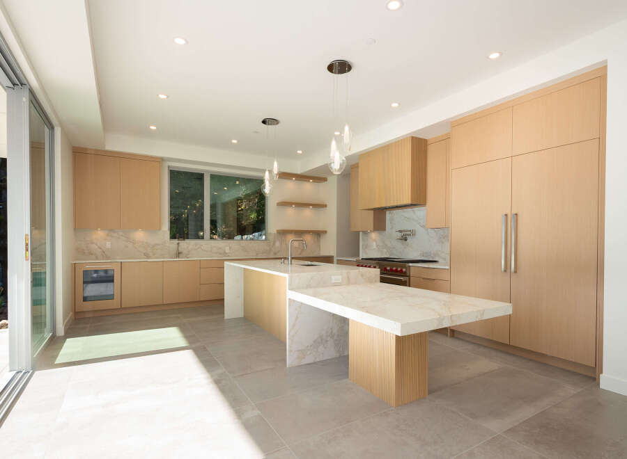 This stunning modern kitchen boasts sleek, light wood cabinetry and a spacious island with a marble countertop, perfect for both cooking and entertaining.