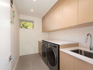 This modern laundry room features sleek cabinetry, a stainless steel sink, and a washer and dryer.