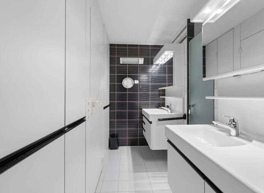 Step into a modern bathroom oasis! This stylish space features sleek white cabinetry, a striking black tiled accent wall, and contemporary fixtures.