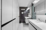 Step into a modern bathroom oasis! This stylish space features sleek white cabinetry, a striking black tiled accent wall, and contemporary fixtures.