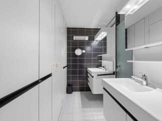 Step into a modern bathroom oasis! This stylish space features sleek white cabinetry, a striking black tiled accent wall, and contemporary fixtures.