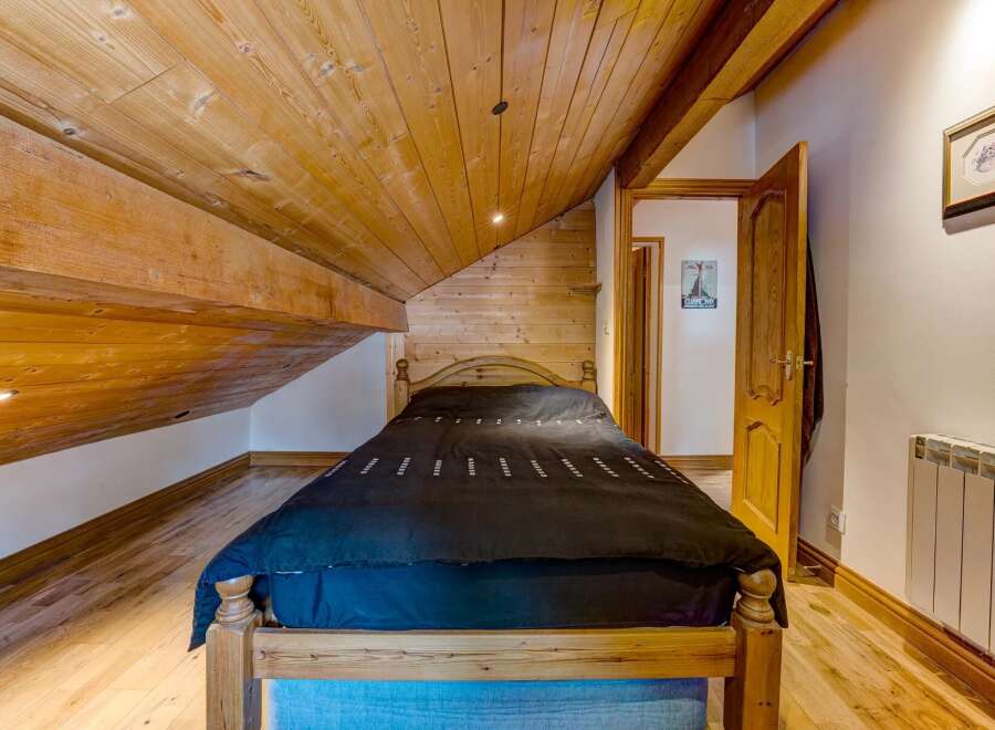 Discover the charm of this cozy bedroom featuring a unique wooden sloped ceiling and exposed beams, creating a warm and inviting atmosphere.