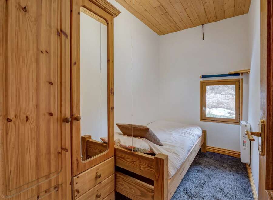 This cozy bedroom features a wooden bed frame and a large wardrobe with a mirror, offering ample storage and a touch of rustic charm.