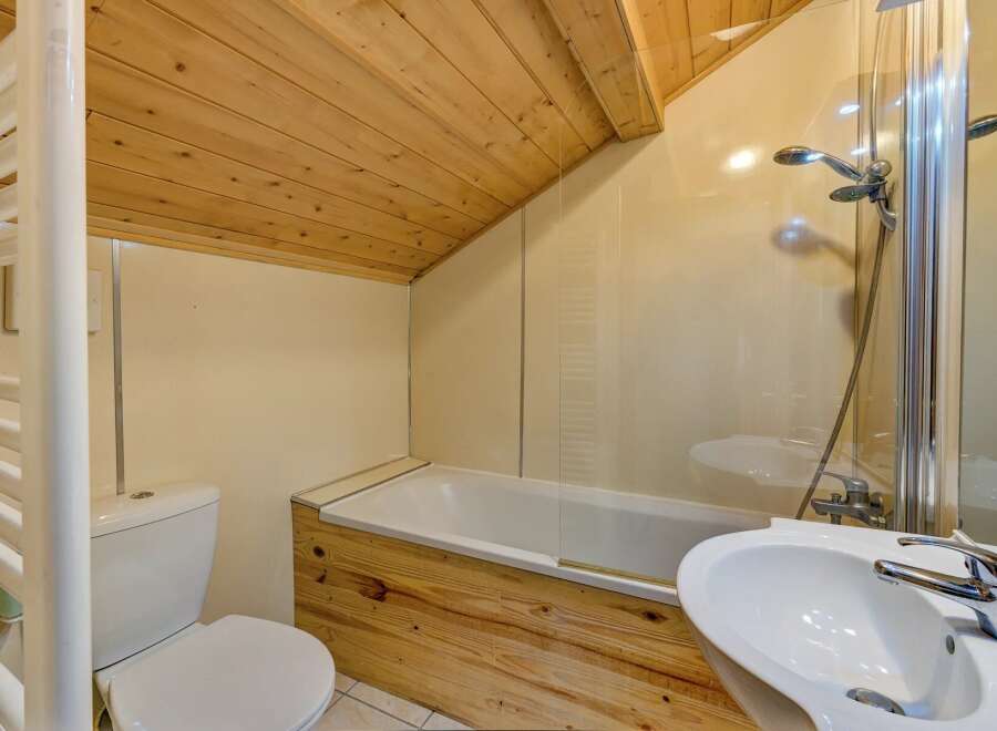 This charming bathroom features a unique wooden ceiling and a stylish wooden accent on the bathtub.