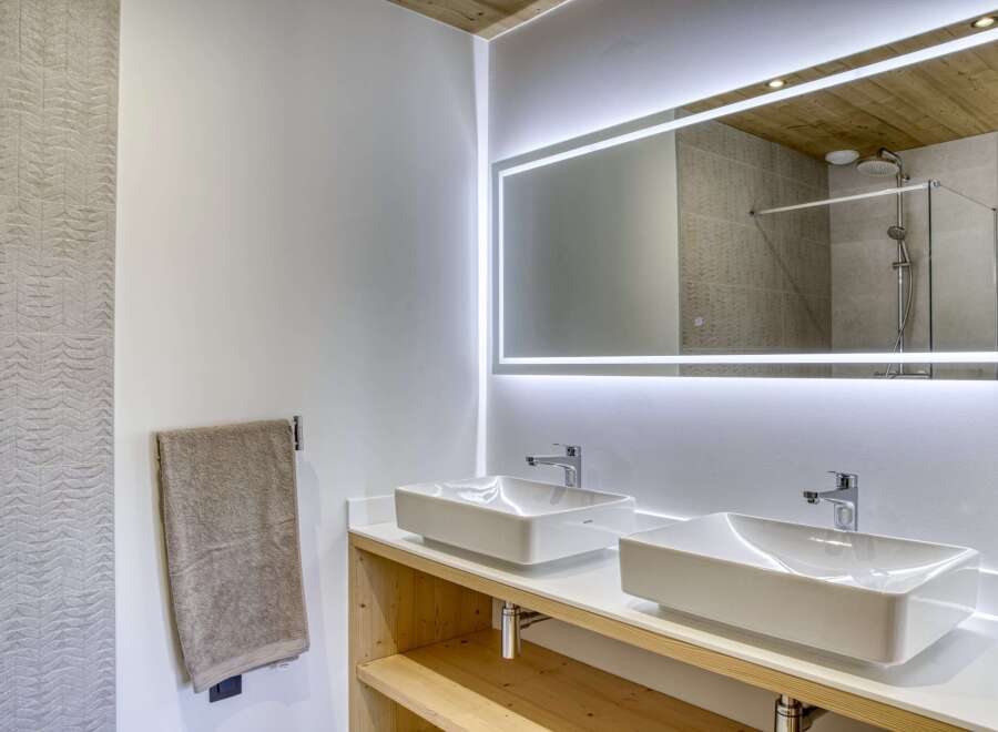 This modern bathroom boasts a sleek design with a double sink vanity and a large, illuminated mirror.