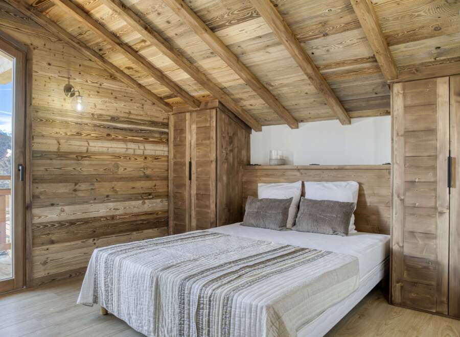 Experience the charm of this cozy bedroom, featuring rustic wooden walls and a sloped ceiling that adds character.