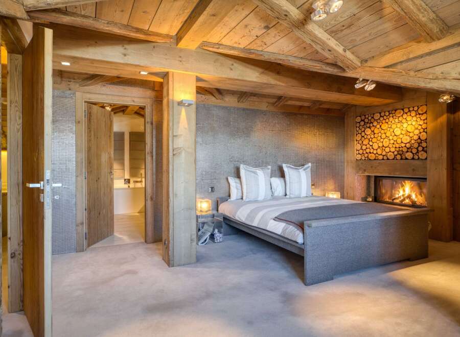 Experience luxury in this stunning bedroom featuring a cozy fireplace and a rustic wooden ceiling.