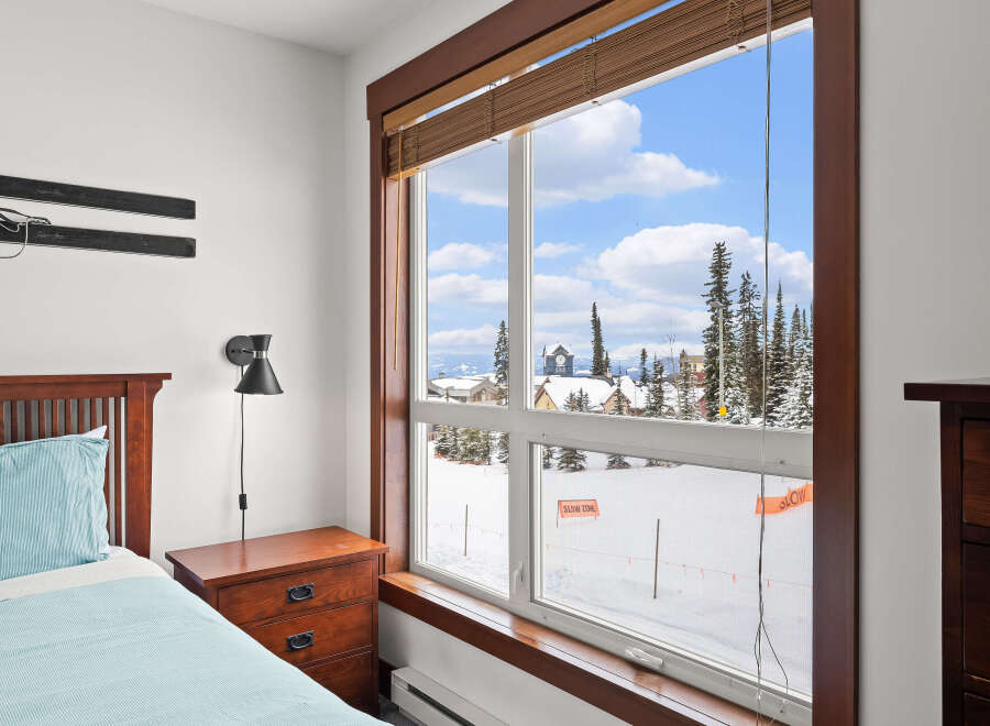 This cozy bedroom offers stunning views of a snowy landscape through a large window.