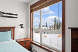 This cozy bedroom offers stunning views of a snowy landscape through a large window.