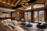 Experience luxurious alpine living in this stunning mountain retreat, featuring a grand living area with a modern fireplace and expansive windows showcasing breathtaking village and mountain views.