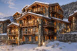 Experience luxury mountain living in this stunning chalet, featuring a rustic stone and timber facade nestled against a snow-covered slope.