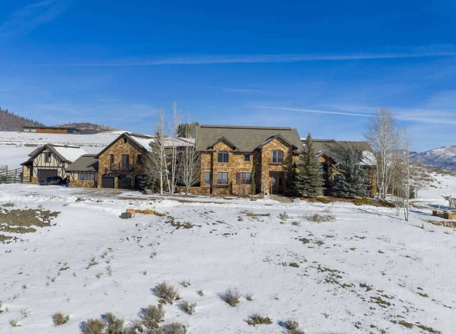 This stunning property showcases a luxurious stone-clad mansion nestled in a serene, snow-covered landscape.