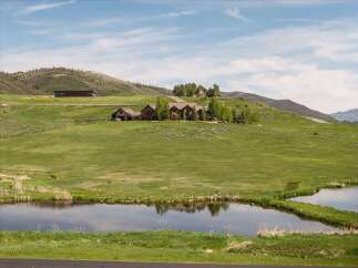 Experience luxurious mountain living in this expansive estate, featuring a stunning main residence and a modern guesthouse nestled on rolling green hills.