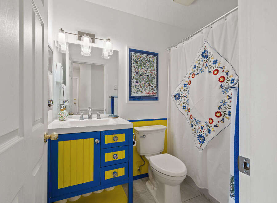 This charming bathroom features a unique blue and yellow vanity, adding a pop of color and personality.