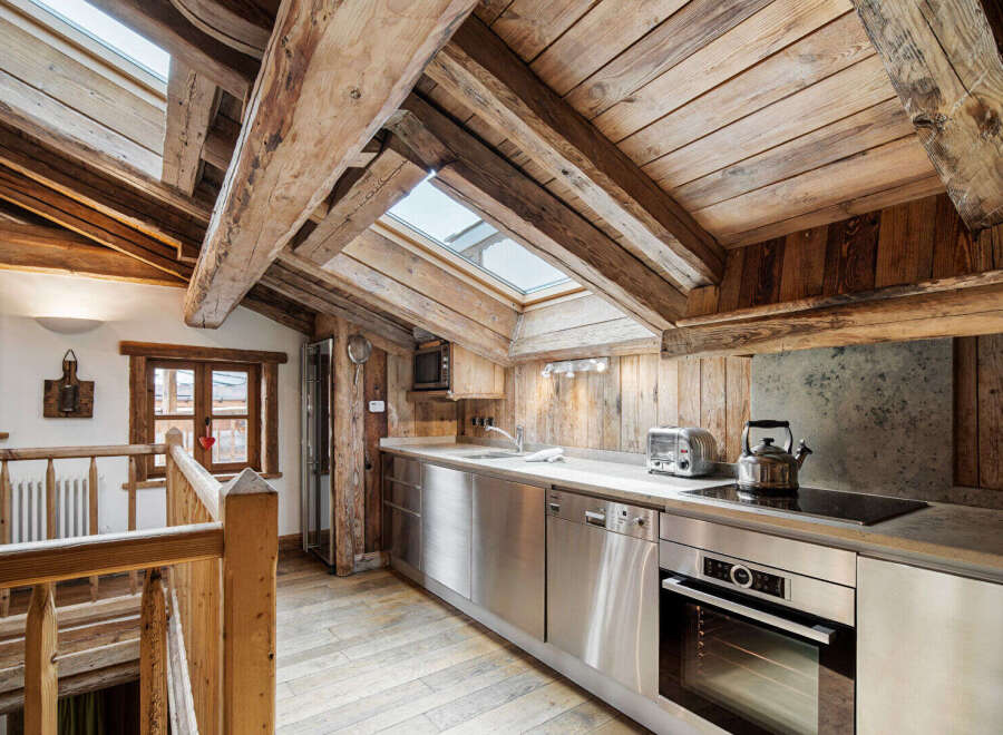 Experience rustic charm in this mountain chalet kitchen, featuring exposed wooden beams and a sloped ceiling with skylights that flood the space with natural light.