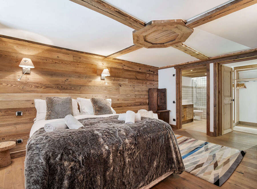 Experience rustic luxury in this charming bedroom, featuring warm wooden walls and exposed beams for a cozy alpine ambiance.