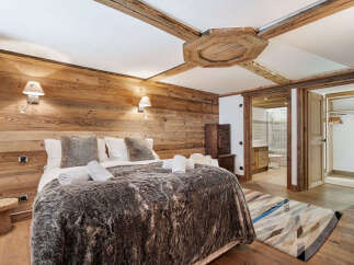 Experience rustic luxury in this charming bedroom, featuring warm wooden walls and exposed beams for a cozy alpine ambiance.