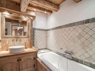 Experience rustic charm in this mountain bathroom, featuring a wooden vanity with a vessel sink and a large mirror framed by exposed beams.