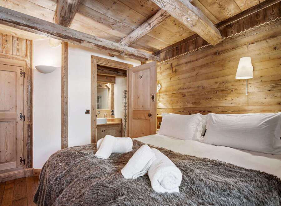Experience rustic charm in this cozy bedroom featuring exposed wooden beams and a plush, fur-covered bed.
