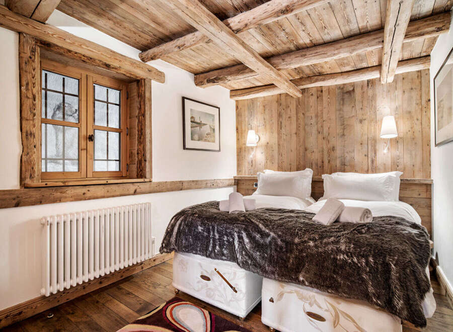 Experience rustic charm in this cozy bedroom featuring exposed wooden beams and a charming window overlooking a snowy landscape.