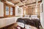 Experience rustic charm in this cozy bedroom featuring exposed wooden beams and a charming window overlooking a snowy landscape.