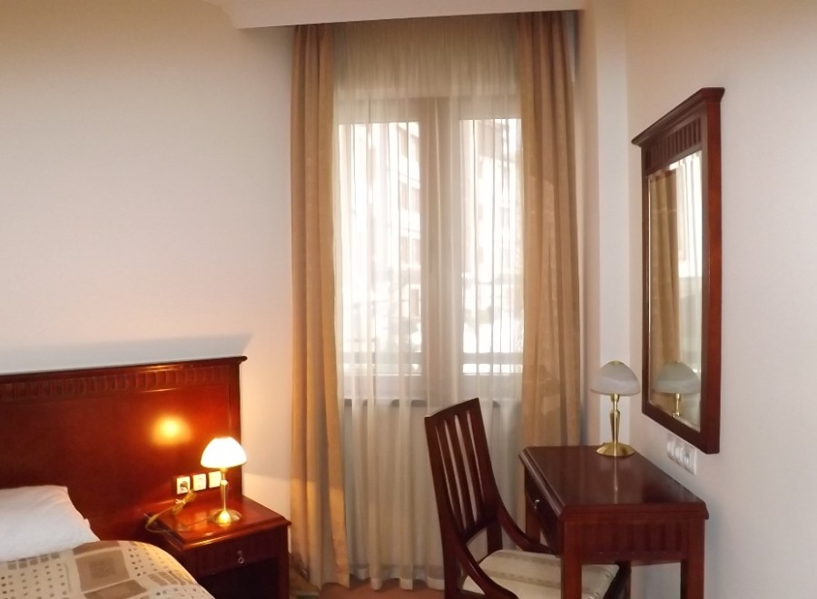 Relax in this well-lit hotel room featuring a comfortable bed, a convenient work desk with chair, and a large mirror.