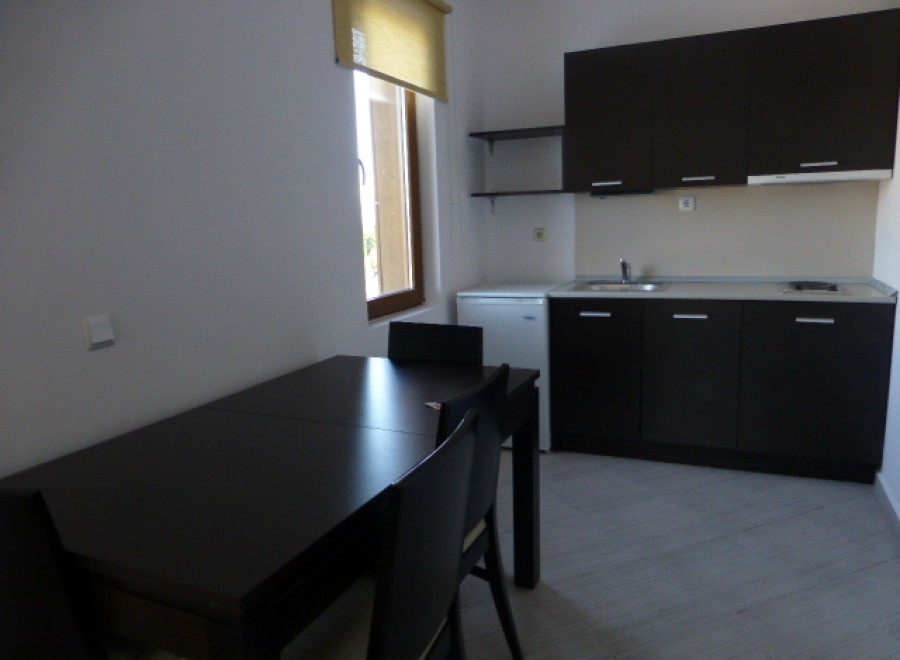 This cozy studio apartment features a well-equipped kitchenette with dark wood cabinets and a small refrigerator.