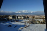 Snow-covered landscape with mountain views and modern apartment buildings.