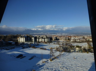 Snow-covered landscape with mountain views and modern apartment buildings.