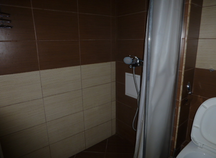 This cozy bathroom boasts a shower with a curtain, modern brown and beige tiles, and a convenient toilet.