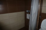 This cozy bathroom boasts a shower with a curtain, modern brown and beige tiles, and a convenient toilet.