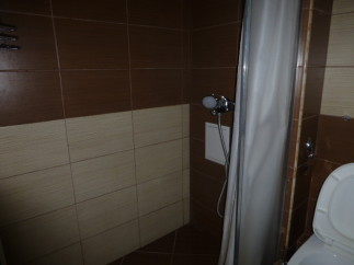 This cozy bathroom boasts a shower with a curtain, modern brown and beige tiles, and a convenient toilet.