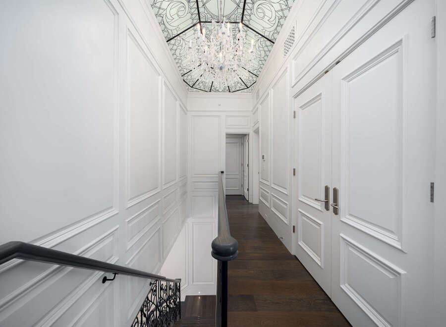 Step into luxury with this stunning hallway, featuring exquisite white paneling and a grand staircase.