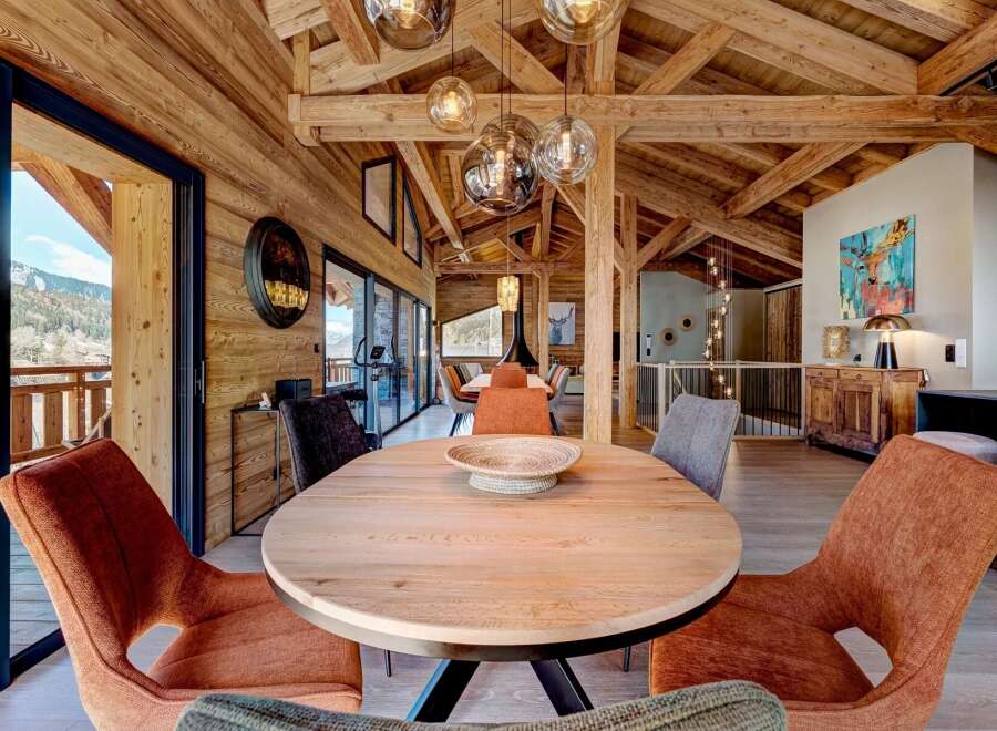 Experience luxury living in this stunning chalet, featuring a warm and inviting interior with exposed wooden beams and a spacious dining area.