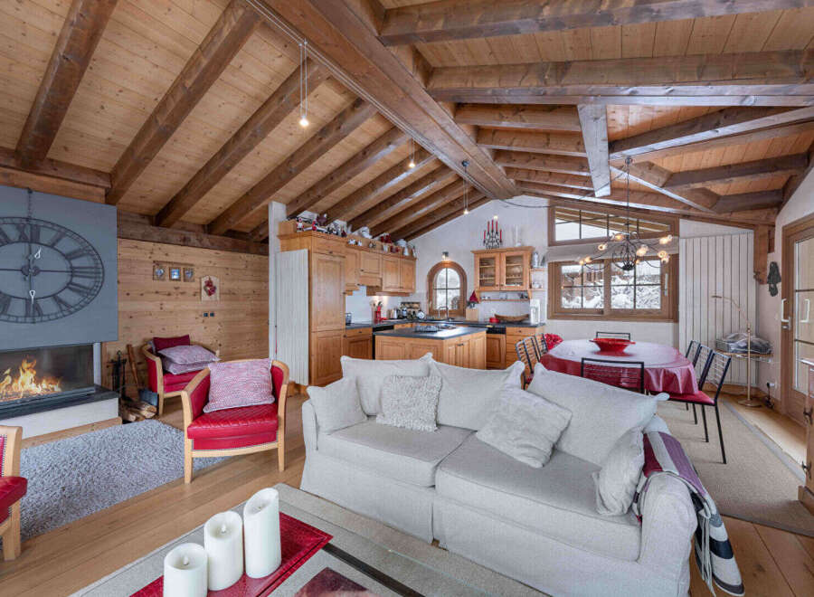 Experience the charm of this stunning chalet, featuring a cozy living room with a fireplace and a rustic wooden ceiling.
