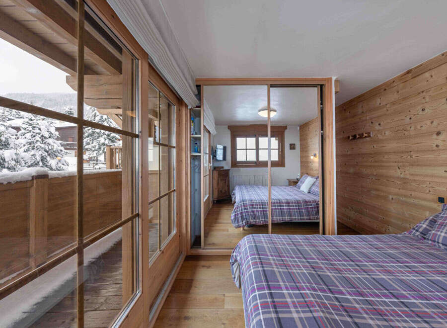 Experience the charm of this cozy bedroom, featuring a stunning view of a snowy landscape through large wooden-framed windows.