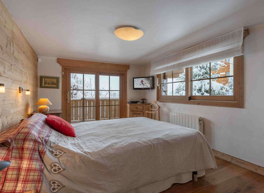 Experience the charm of this cozy bedroom, featuring a warm wooden interior and a stunning view of a snowy landscape.