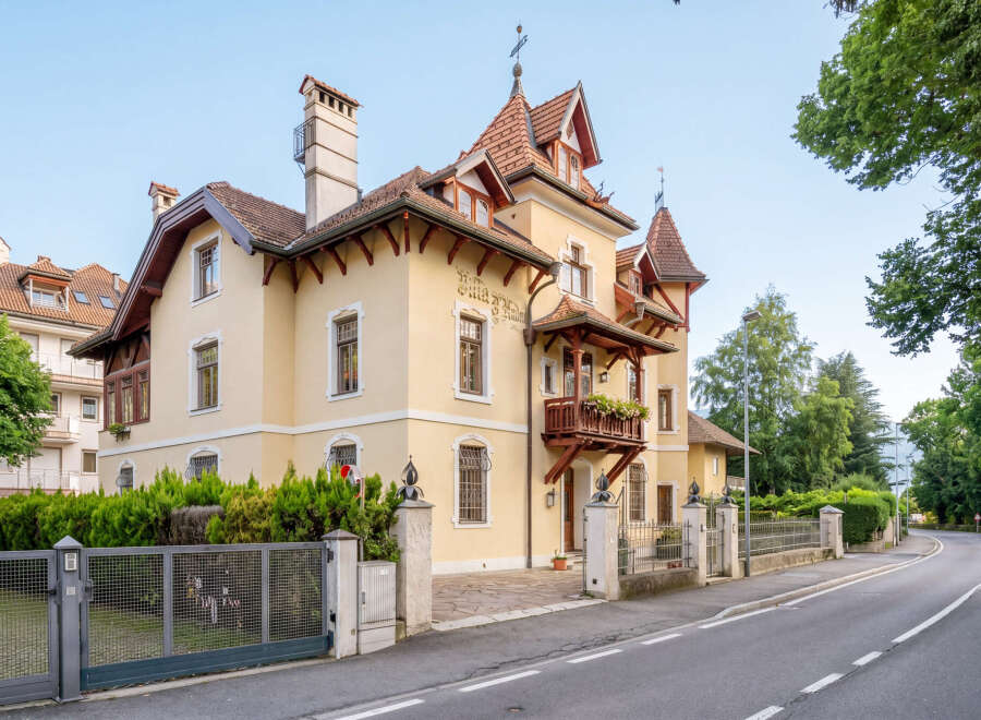 Charming yellow villa with intricate architectural details and a welcoming balcony adorned with flowers.