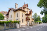 Charming yellow villa with intricate architectural details and a welcoming balcony adorned with flowers.