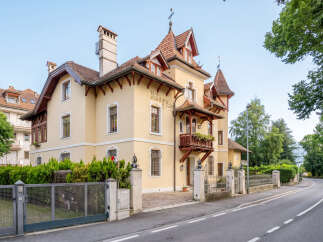 Charming yellow villa with intricate architectural details and a welcoming balcony adorned with flowers.