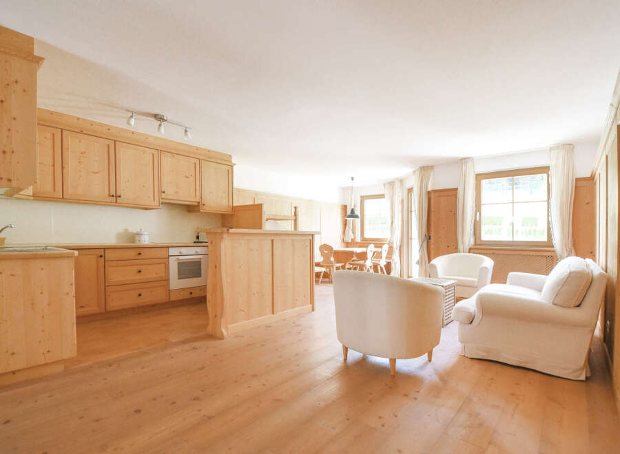 Experience rustic charm in this inviting open-plan living space, featuring a fully equipped wooden kitchen and a cozy seating area with plush white armchairs.