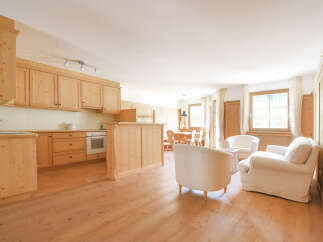 Experience rustic charm in this inviting open-plan living space, featuring a fully equipped wooden kitchen and a cozy seating area with plush white armchairs.