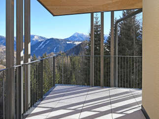 Experience breathtaking mountain views from this modern balcony, featuring a sleek metal railing and a warm wooden ceiling.