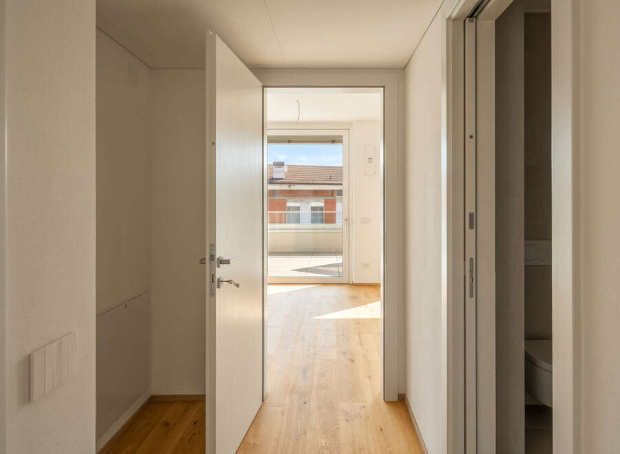 Step into a bright and airy hallway with gleaming hardwood floors that lead to a spacious balcony overlooking a charming neighborhood.