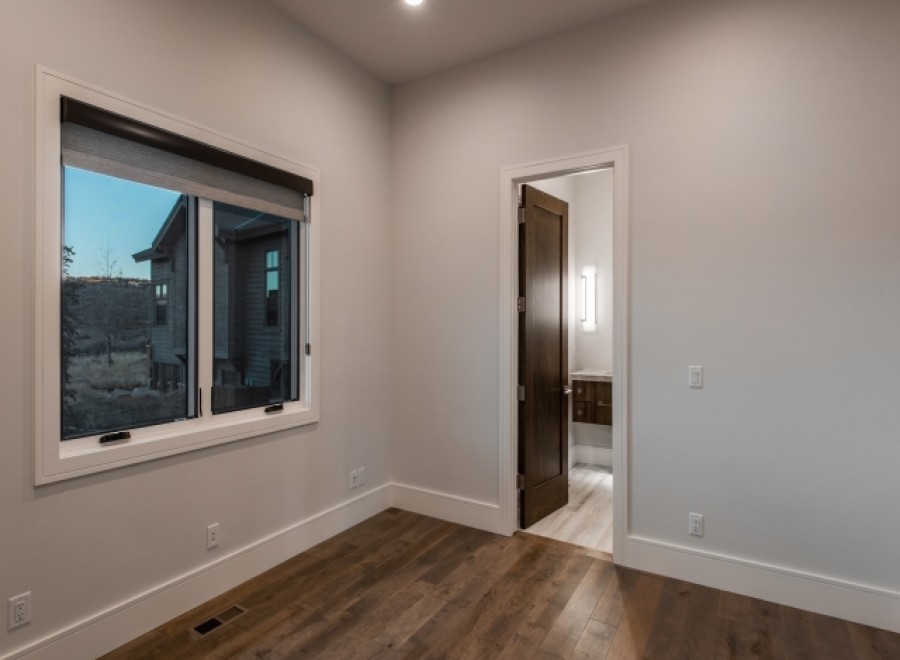 This stunning bedroom boasts a large window with a modern roller shade, offering ample natural light and views of the surrounding landscape.