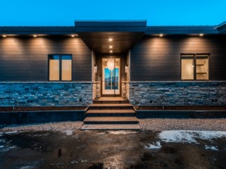 This stunning modern home boasts a sleek exterior with dark siding, stone accents, and a welcoming entryway.